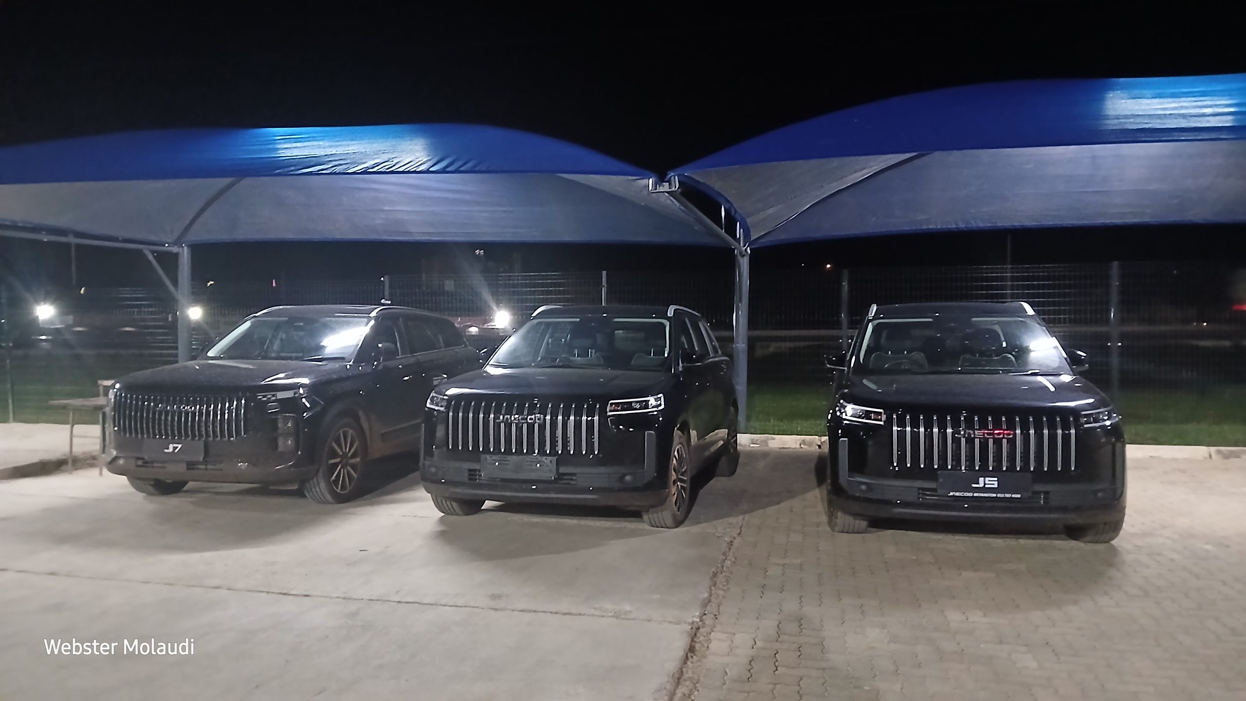 Three black SUVs parked under canopy at night
