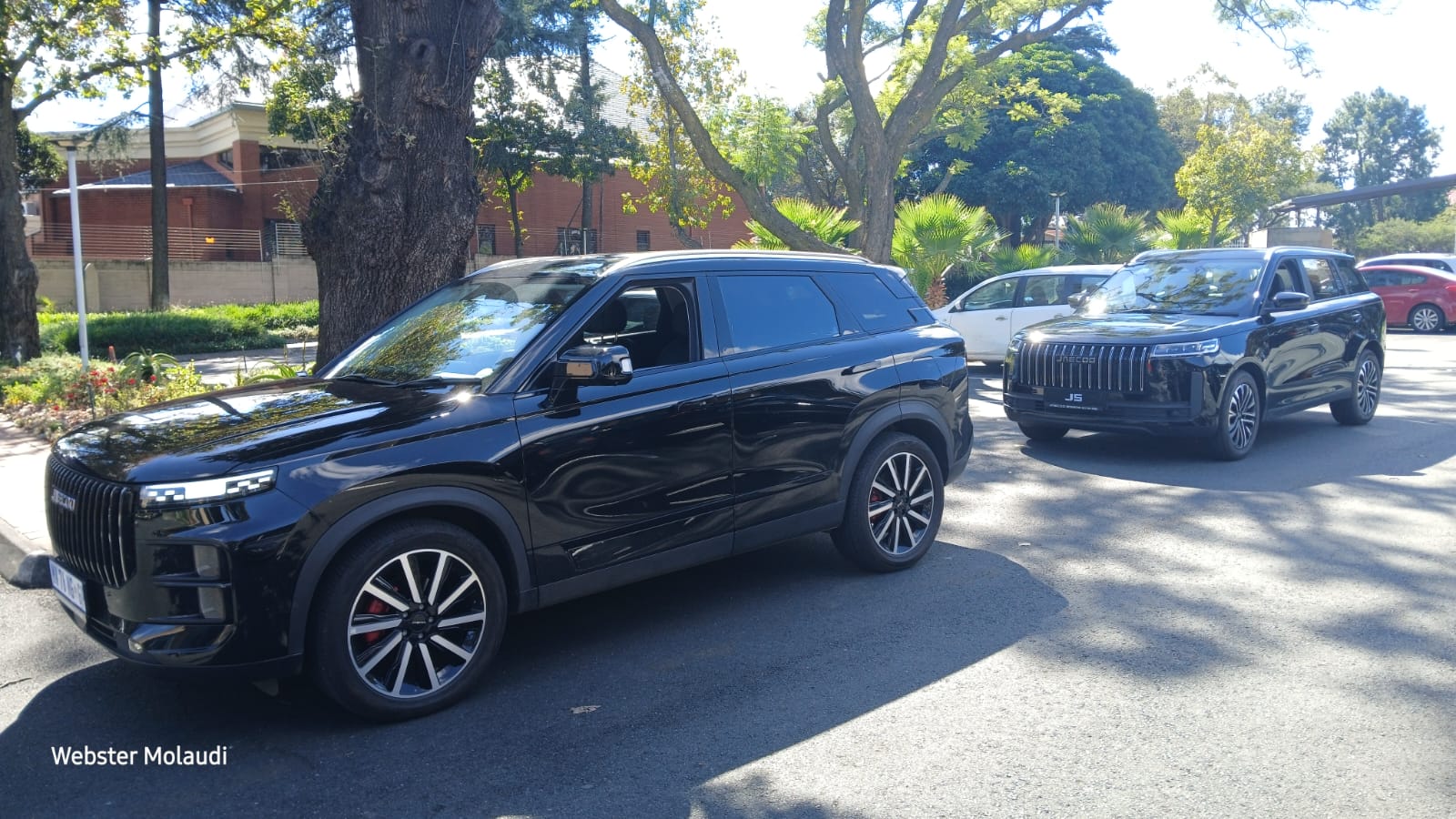 Two black SUVs parked on sunny street