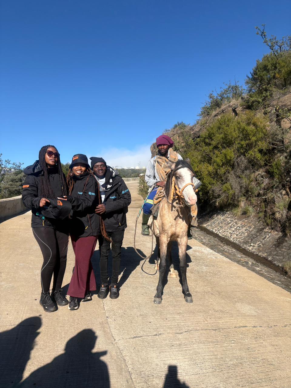 Three women posing beside man on horse