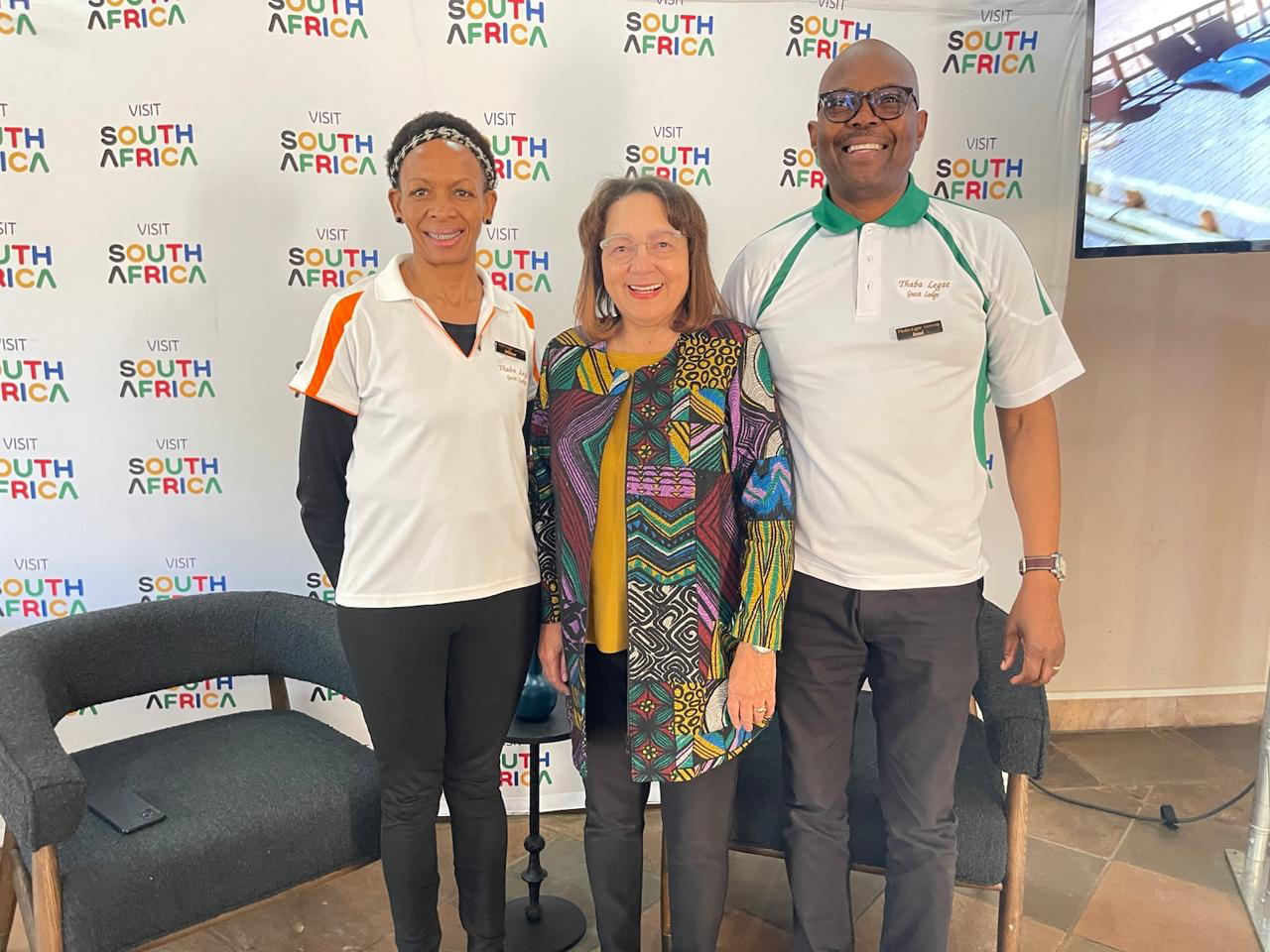 Three people pose before Visit South Africa backdrop