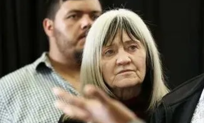 Older woman with long hair, serious expression.