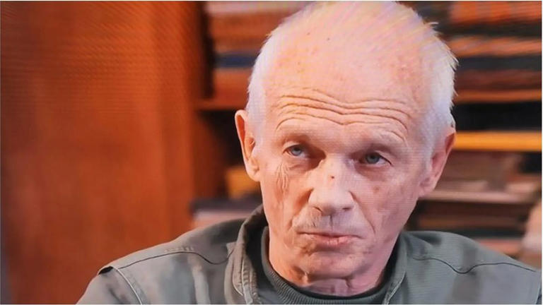 Older man gazing thoughtfully indoors.