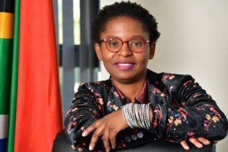 Woman with glasses, South African flag in background