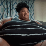 Person sitting on couch with patterned curtains behind.