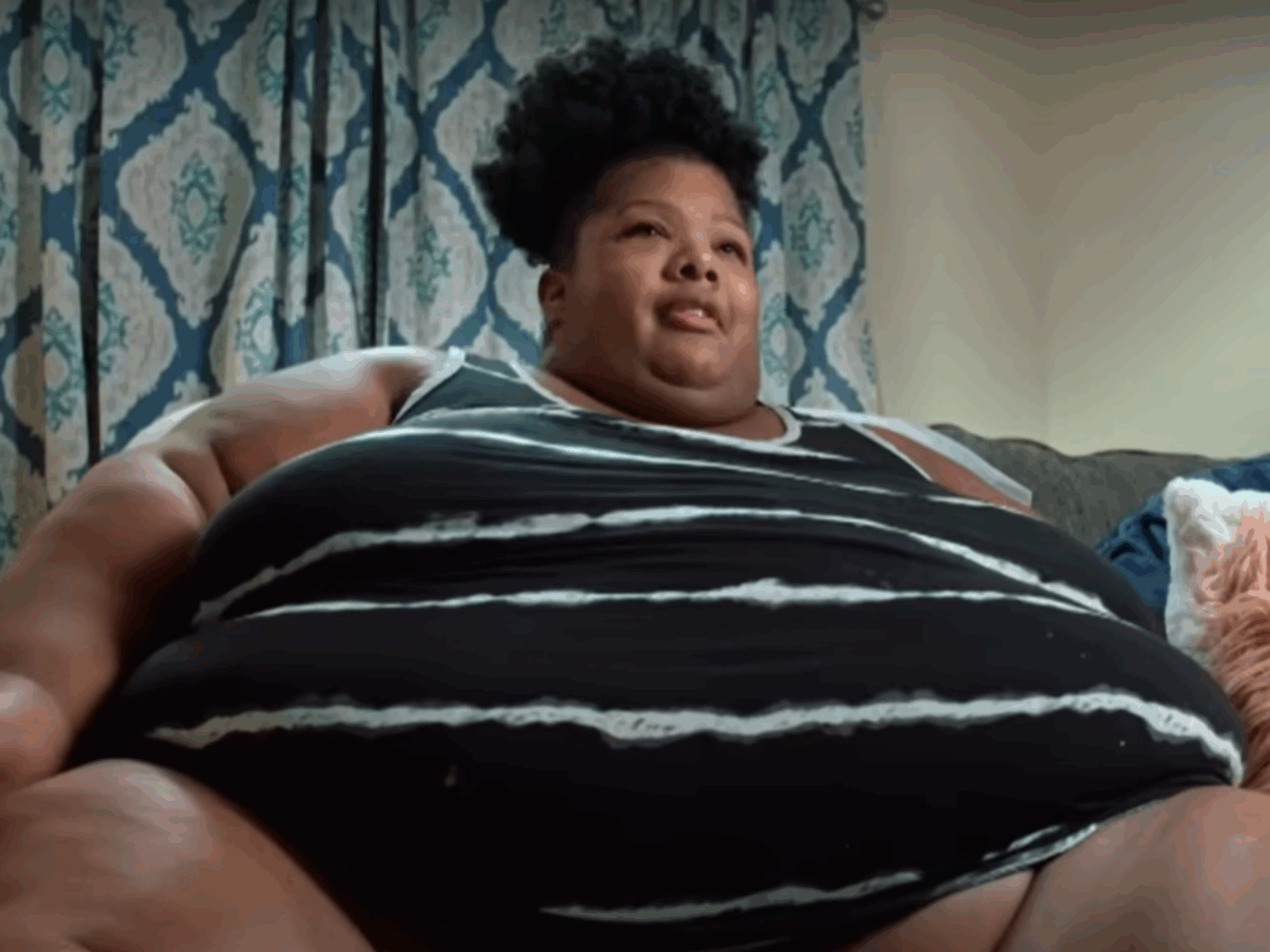 Person sitting on couch with patterned curtains behind.