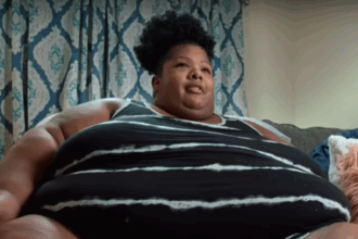 Person sitting on couch with patterned curtains behind.