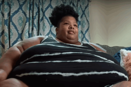 Person sitting on couch with patterned curtains behind.