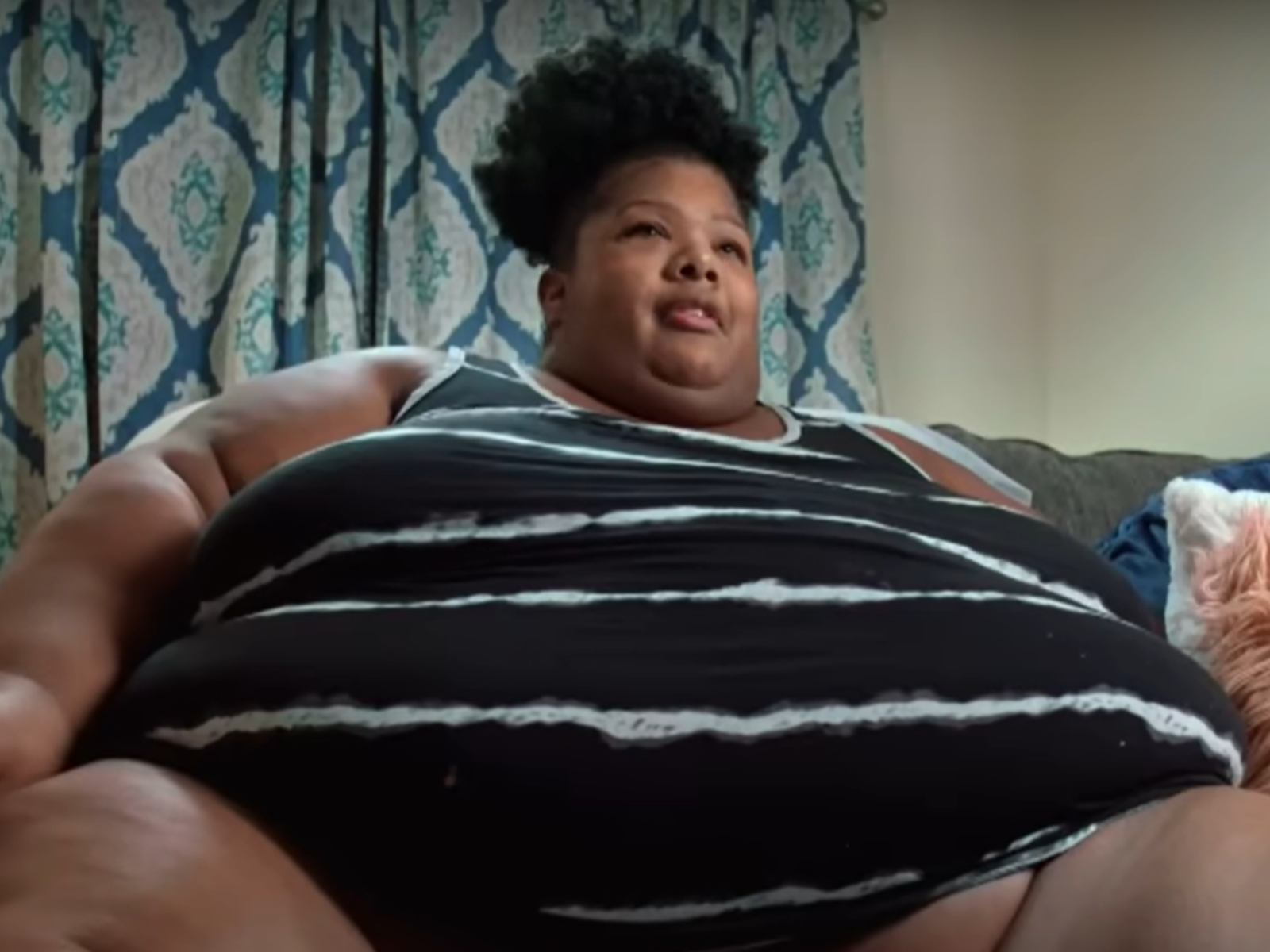 Person sitting on couch with patterned curtains behind.