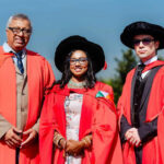 Three graduates in red robes at ceremony.