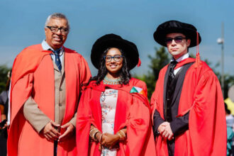 Three graduates in red robes at ceremony.