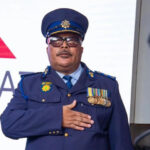 Police officer with medals salutes in formal uniform.