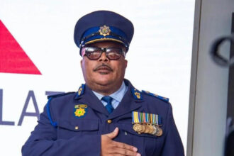Police officer with medals salutes in formal uniform.