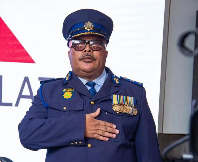 Police officer with medals salutes in formal uniform.