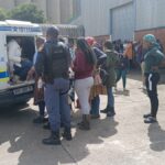 Police van with people detained outside building.