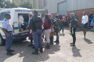 Police van with people detained outside building.