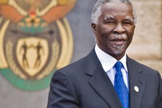 Man in suit standing before South African emblem.