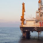 Offshore oil rig with supply vessel at sunset.