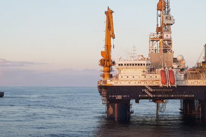 Offshore oil rig with supply vessel at sunset.