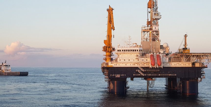 Offshore oil rig with supply vessel at sunset.