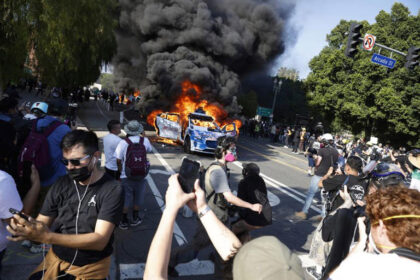 Protesters surround burning car in street demonstration.