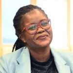 Smiling person wearing glasses and blue blazer.