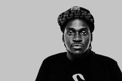 Man in cap and black shirt, grey background.