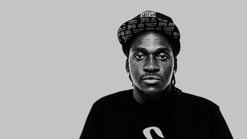 Man in cap and black shirt, grey background.