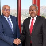 Two executives shaking hands in office setting.