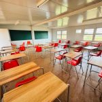Empty classroom with red chairs and wooden desks.