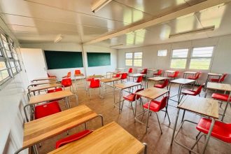 Empty classroom with red chairs and wooden desks.
