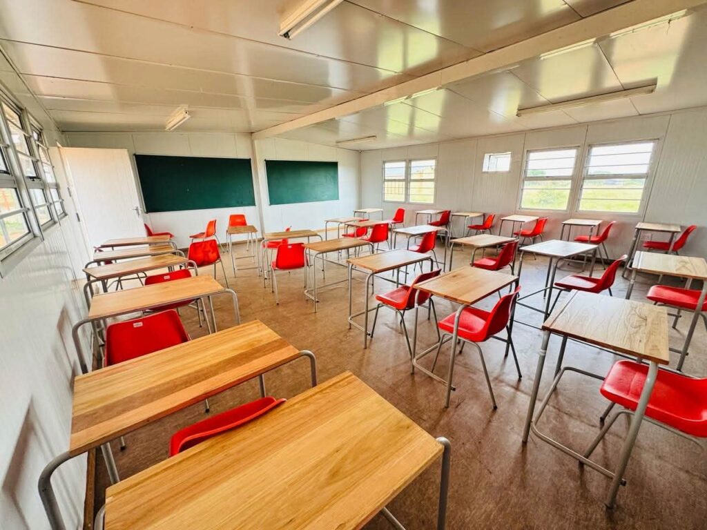 Empty classroom with red chairs and wooden desks.