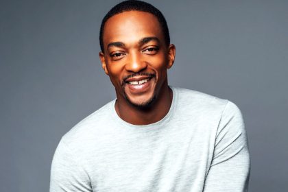 Smiling man in grey sweater, neutral background.