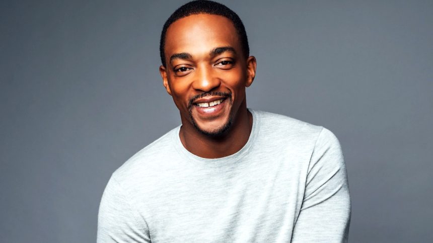 Smiling man in grey sweater, neutral background.
