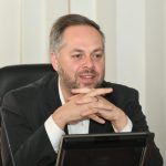 Man sitting at desk with microphone and water bottle.