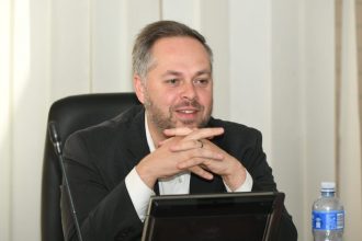 Man sitting at desk with microphone and water bottle.