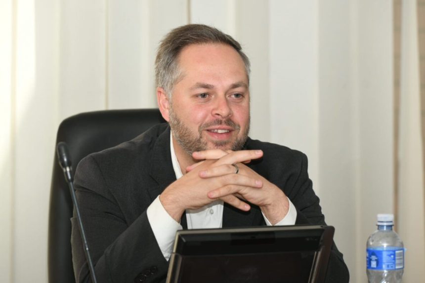 Man sitting at desk with microphone and water bottle.