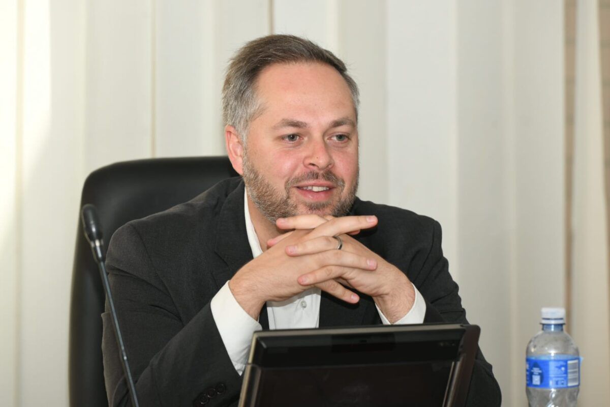 Man sitting at desk with microphone and water bottle.