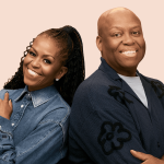 Two people smiling back-to-back, wearing denim and cardigan.