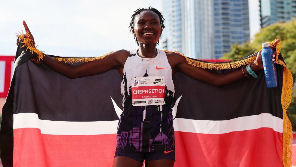 Runner celebrates with Kenyan flag and medal.