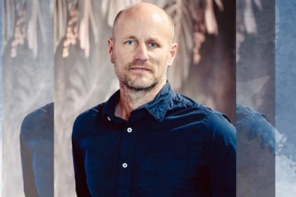 Man in blue shirt stands against blurred background.