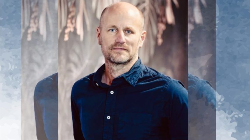 Man in blue shirt stands against blurred background.