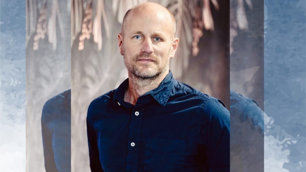 Man in blue shirt stands against blurred background.