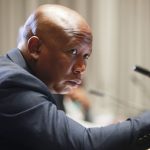 Person speaking at microphone during formal event.