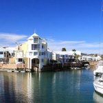 Scenic waterfront with colourful houses and docked sailboat.