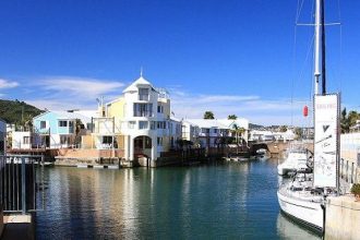 Scenic waterfront with colourful houses and docked sailboat.
