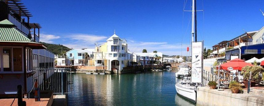 Scenic waterfront with colourful houses and docked sailboat.