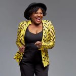 Smiling woman in yellow patterned jacket, black hat.