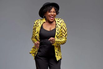 Smiling woman in yellow patterned jacket, black hat.