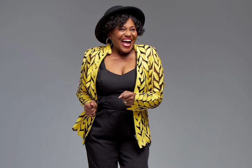 Smiling woman in yellow patterned jacket, black hat.