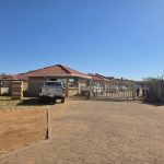 Gated house with parked bakkie in dry landscape.